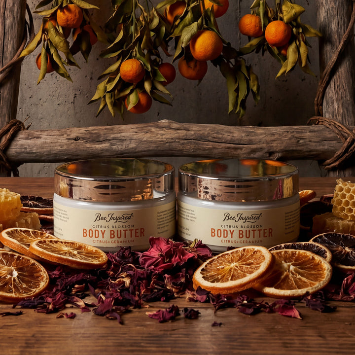 Two jars of body butter on a wooden surface with oranges and honeycomb.