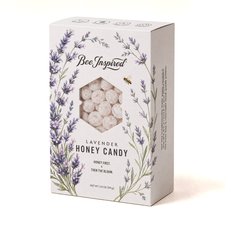 A boxed product labeled Bee Inspired Lavender Honey Candy, shown on a plain light beige background. The white box features lavender floral illustrations and a clear window revealing round pale candy pieces inside.
