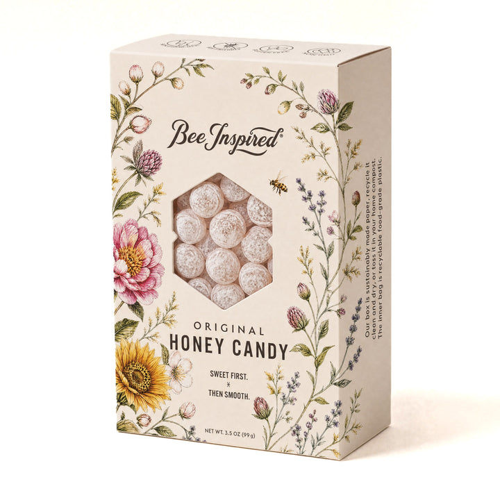 A rectangular cream-colored product box for Bee Inspired Original Honey Candy, decorated with floral illustrations and featuring a hexagonal window showing the white, frosted candy balls inside.