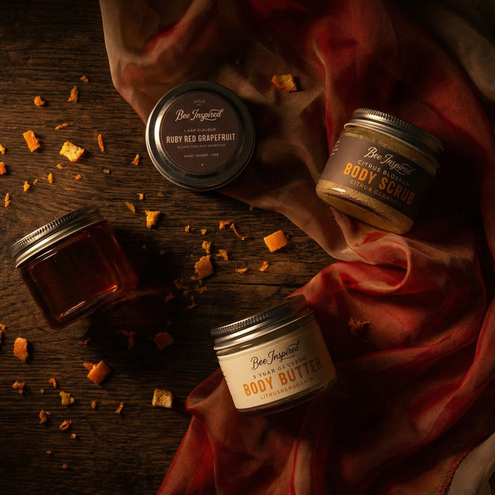 Four jars of Bee Inspired body products on a wooden surface with a red cloth.