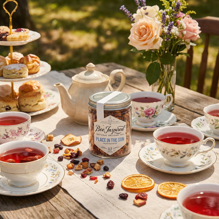 Tea party setup with tea cups, teapot, and a jar of 'Bee Inspired' tea on a wooden table outdoors.