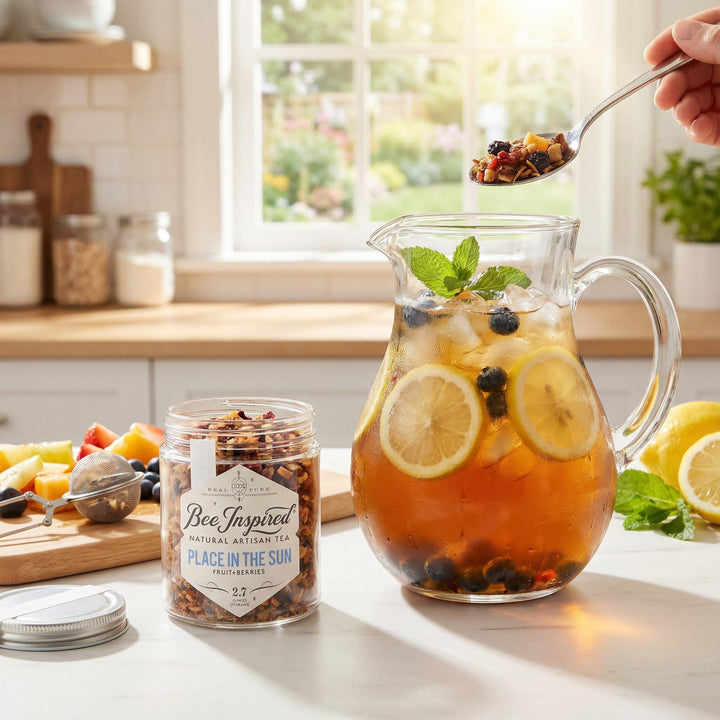 Punch bowl with fruit and tea, jar of Bee Inspired tea, and spoonful of fruit on a kitchen counter.