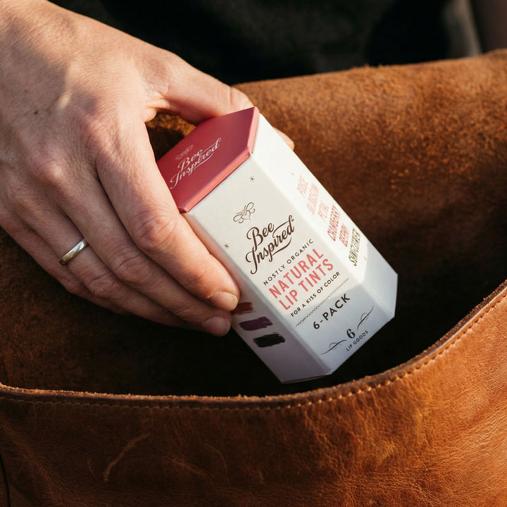 Hand holding a box of 'Bee Inspired' lip tint packaging against a brown leather background