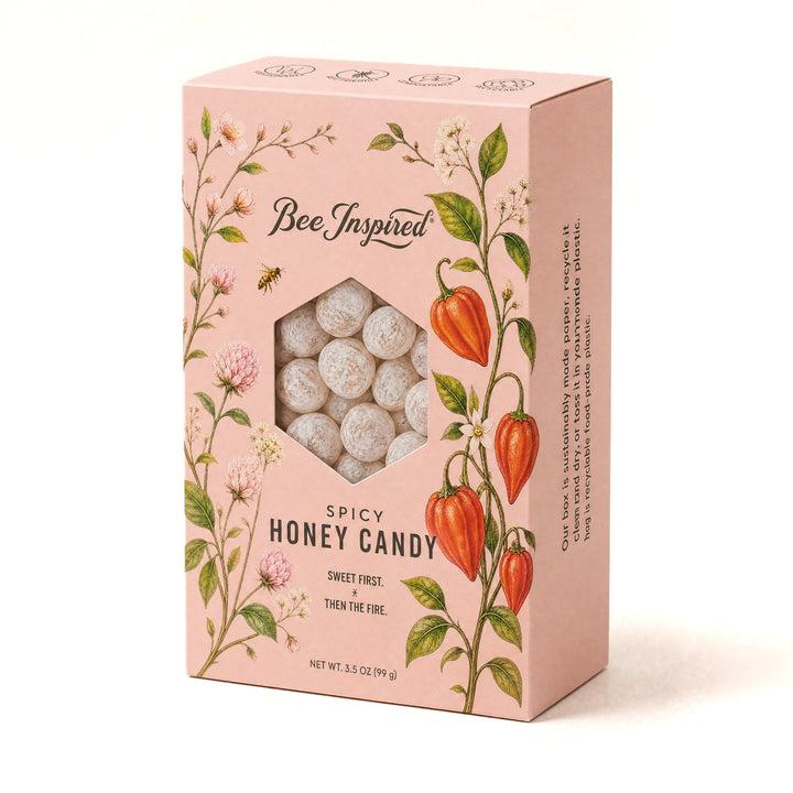 A pink rectangular box of Bee Inspired Spicy Honey Candy, featuring botanical illustrations of flowers, leaves, and chili peppers, with a clear window showing the white, round candy inside.