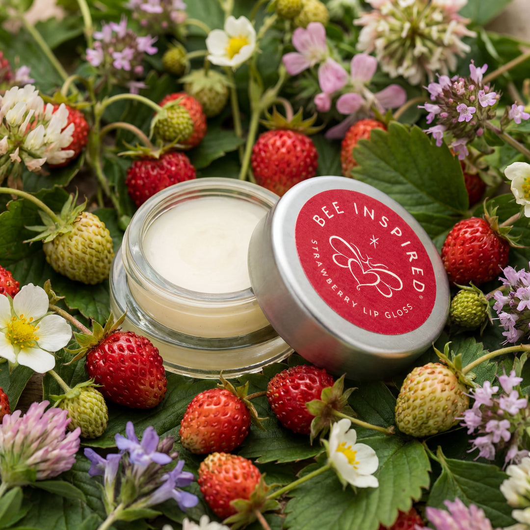 Lip gloss container labeled 'Bee Inspired' surrounded by strawberries and flowers