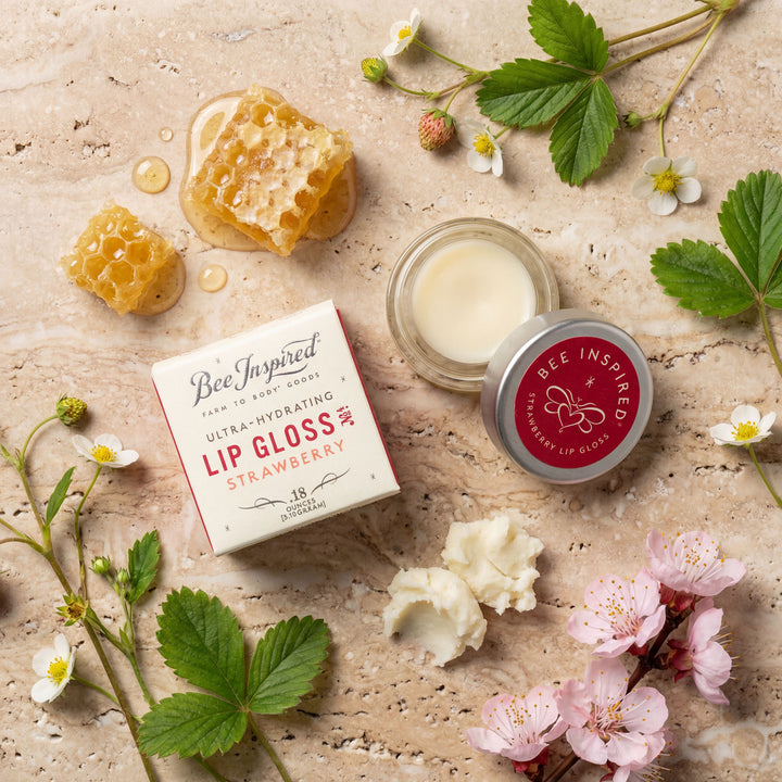 Bee Inspired lip gloss with packaging on a natural background with flowers and honeycomb.